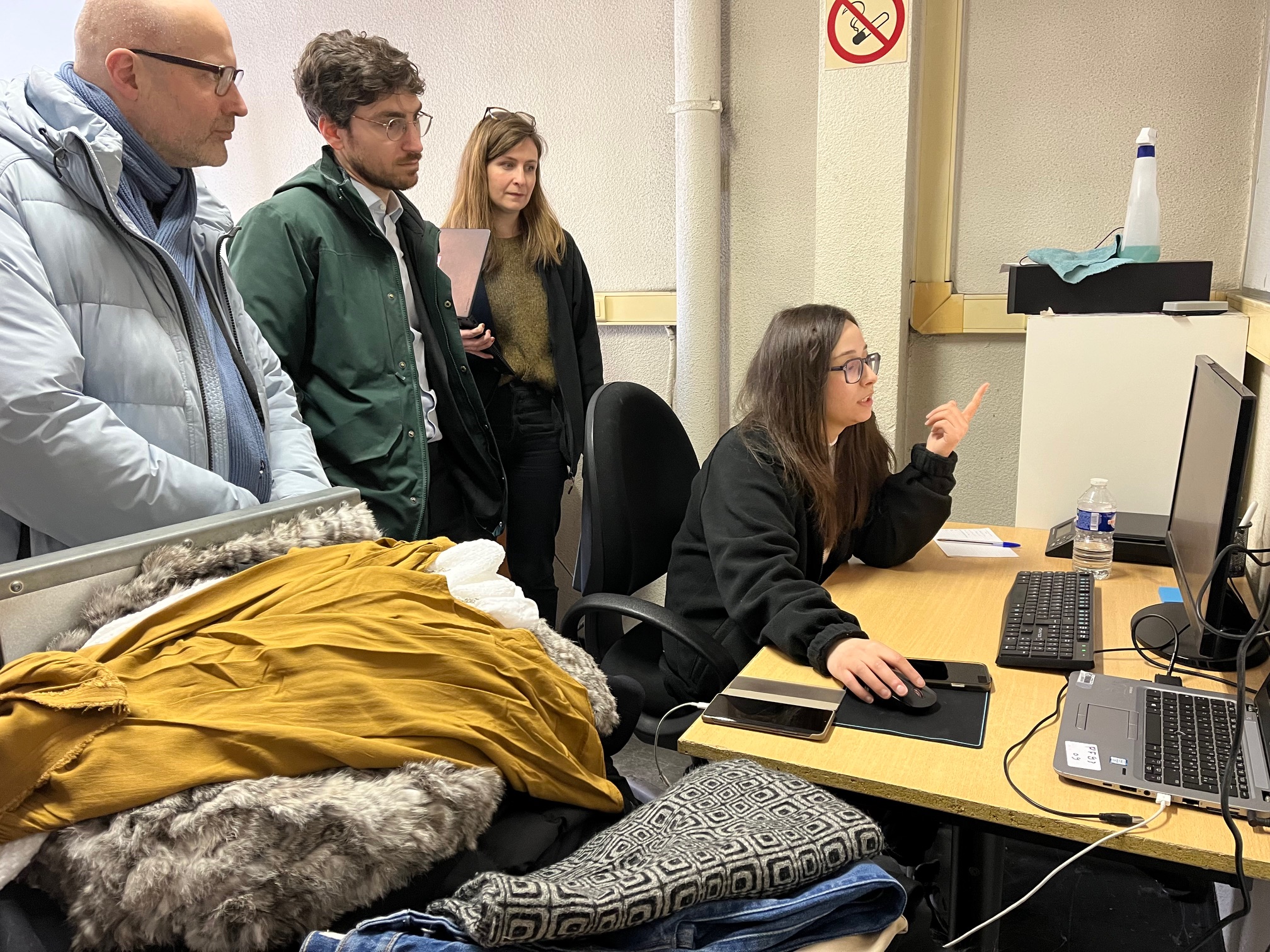 Fatma montre les différentes étapes de la mise en ligne de vêtements sur la boutique en ligne au délégué ministériel à l'ESS, Maxime Baduel, et à son équipe. Crédit : Carenews. 