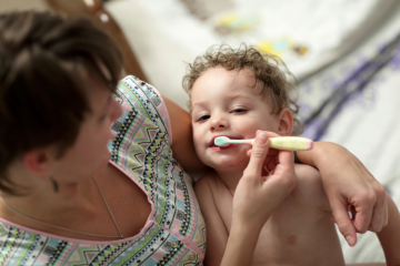 Une femme tient un jeune enfant dans ses bras et lui brosse les dents